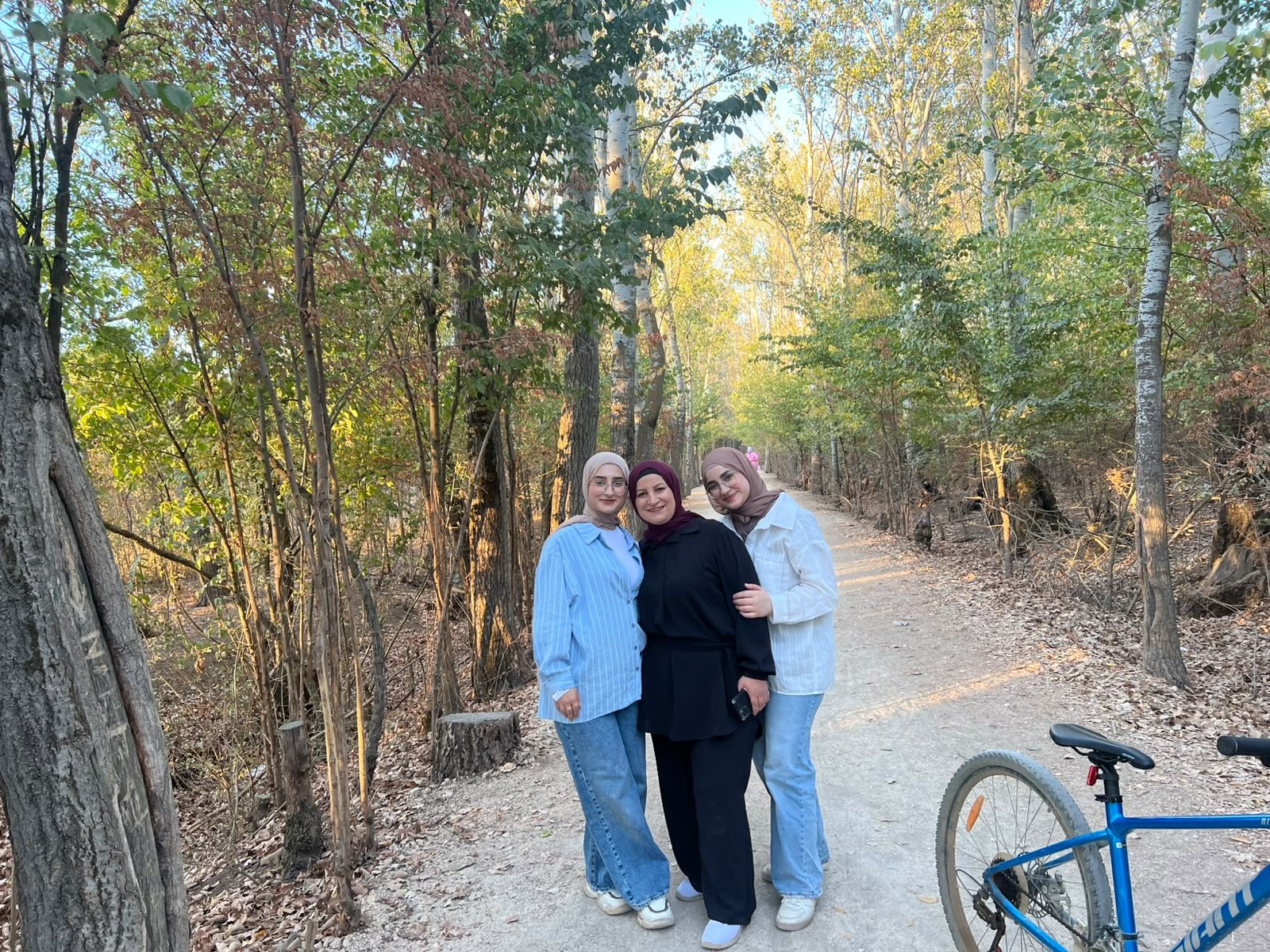 Fatima with her family on a sunlit forest path, the three of them standing arm in arm.