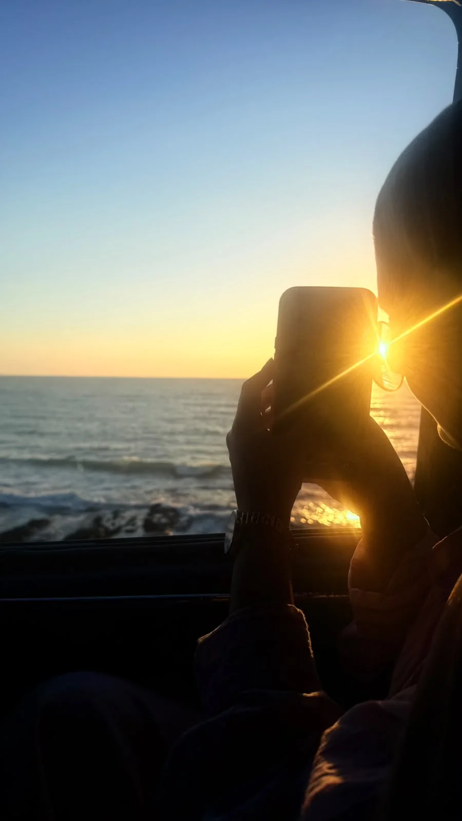 A silhouette photographing the sun as it sets over the sea.