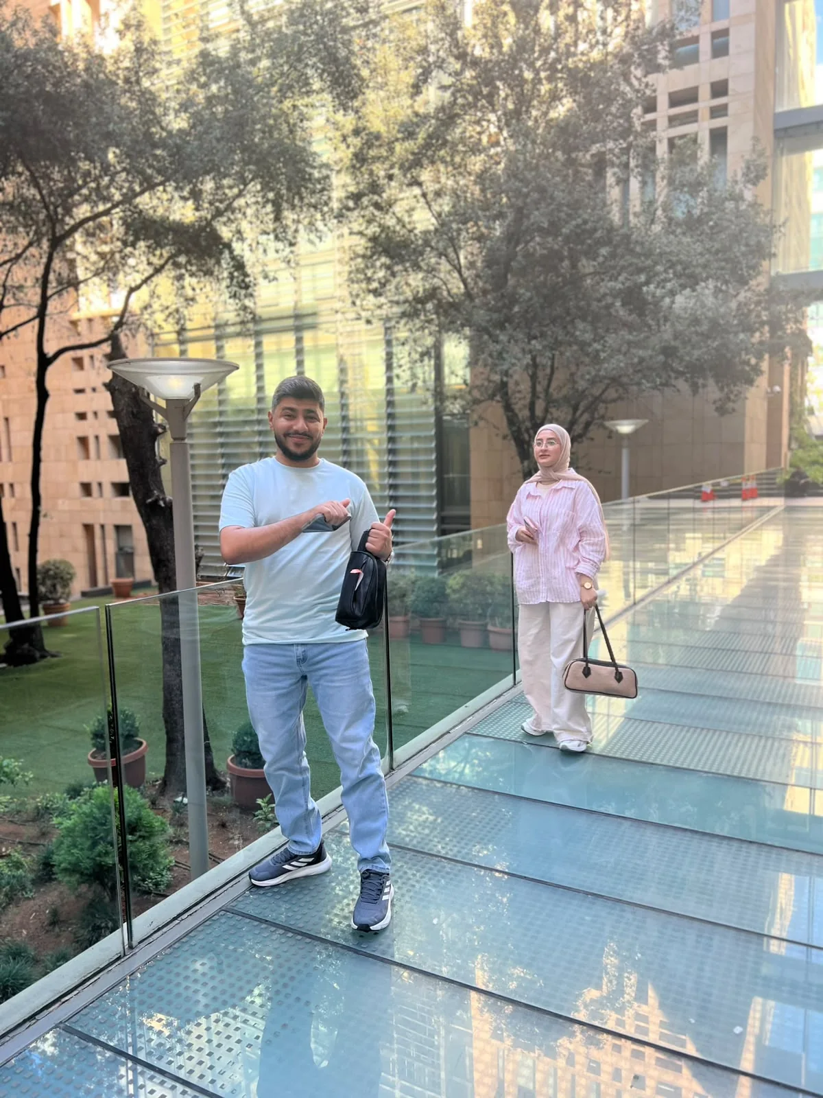 On the glass walkway: a thumbs-up in front, Fatima walking up behind.